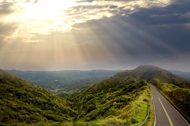 Dağlar ve bir yol üstündeki bulutlar ve gökyüzü arka plan dağda kıvrımlarına üzerinde güneş ışınları ile güzel günbatımı