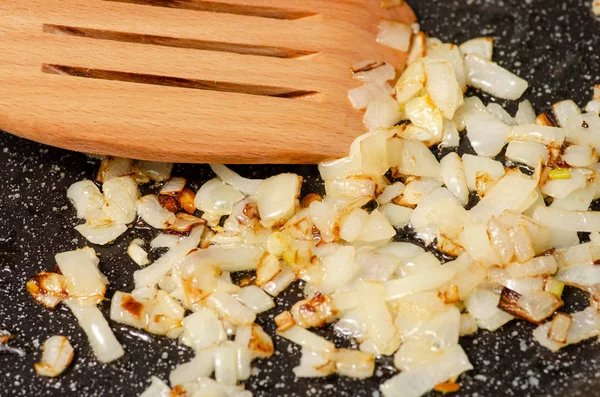 Жареный лук на сковородке деревянная кухонная лопатка — стоковое фото
