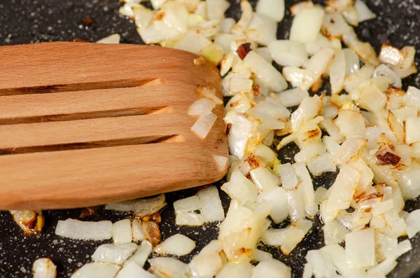 Жареный лук на сковородке деревянная кухонная лопатка — стоковое фото