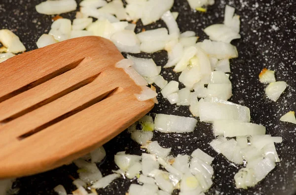 Cebollas fritas en una sartén espátula de cocina de madera —  Fotos de Stock