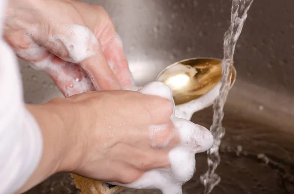 Gąbka do mycia naczynia łyżkę w rękach — Zdjęcie stockowe