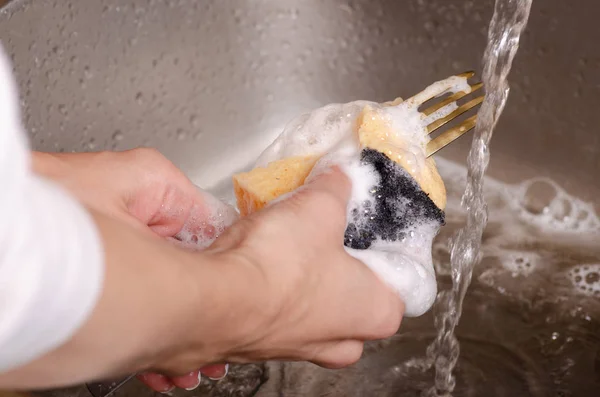 Éponge pour laver les ustensiles une fourchette dans les mains — Photo