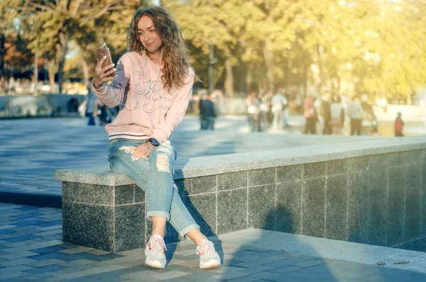 Mulher sentada jeans sweatshirt tênis assistir smartphone fone de ouvido do telefone móvel — Fotografia de Stock