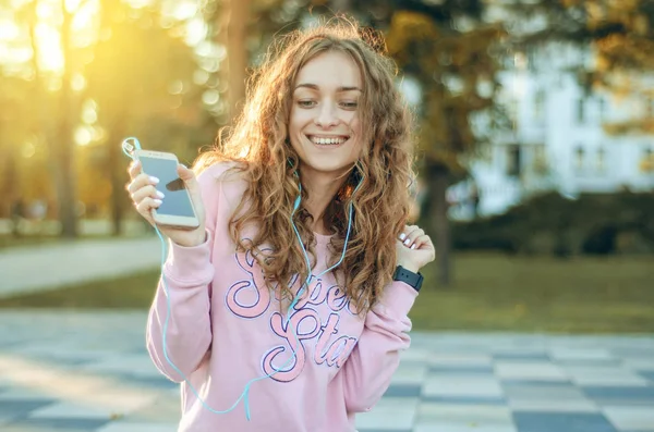 Woman sitting jeans sweatshirt sneakers watch smartphone mobile phone headphones selfie happy smiling