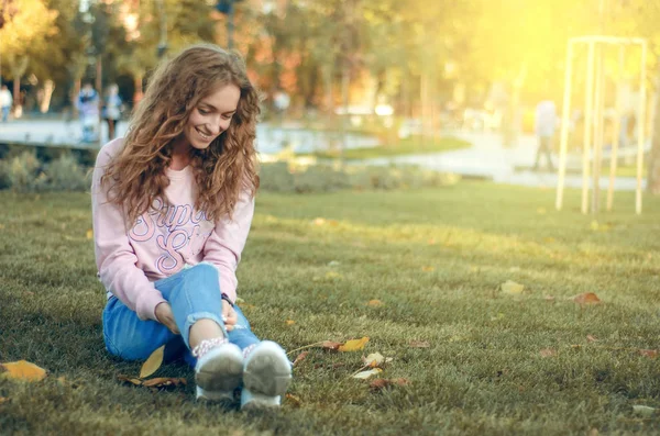 Hermosa mujer en jeans y una sudadera en las zapatillas de calle otoño parque sonriendo feliz —  Fotos de Stock
