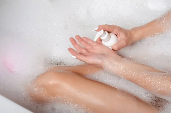 Schöne Frau in Badeschaum Schönheit Gesundheit Beine in der Hand weiße Flasche kosmetische Gel Duschshampoo — Stockfoto