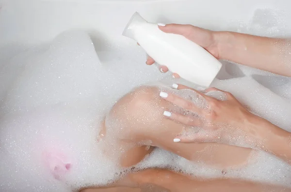 Mulher bonita em espuma de banho beleza saúde pernas na mão whitw garrafa gel cosmético shampoo chuveiro — Fotografia de Stock