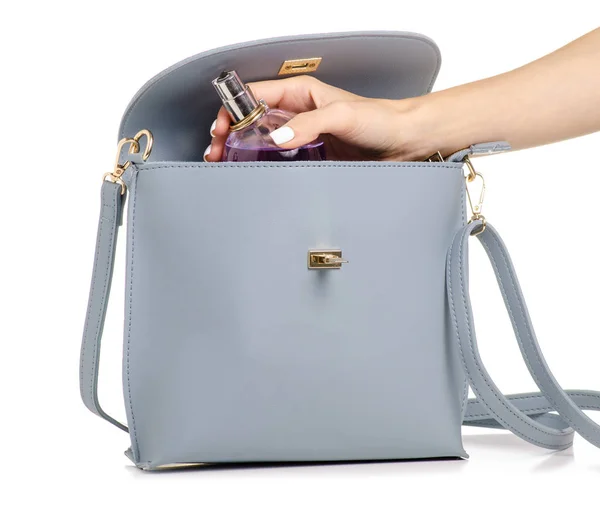 Une main mettre parfum cosmétique dans le sac à main en cuir gris bleu féminin — Photo