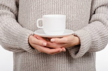 Bir beyaz Kupası ve fincan tabağı, elinde tutan kazaklı genç kadın sıcak kahve içme.