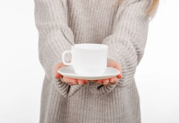 Jeune femme en pull tenant une tasse blanche et une soucoupe dans les mains, buvant du café chaud . — Photo