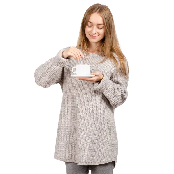Mujer joven en suéter sosteniendo una taza blanca y platillo en las manos, bebiendo café caliente . — Foto de Stock