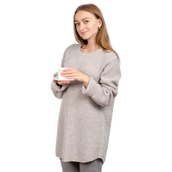 Jovem mulher em suéter segurando uma xícara branca e pires nas mãos, bebendo café quente . — Fotografia de Stock