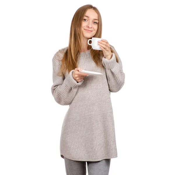 Mujer joven en suéter sosteniendo una taza blanca y platillo en las manos, bebiendo café caliente . — Foto de Stock