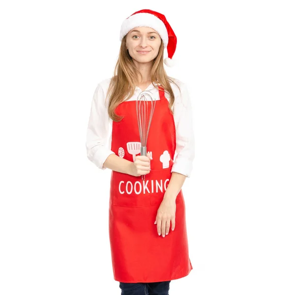 Una mujer en un delantal rojo sombrero de santa en las manos de una corola batidor de cocina —  Fotos de Stock
