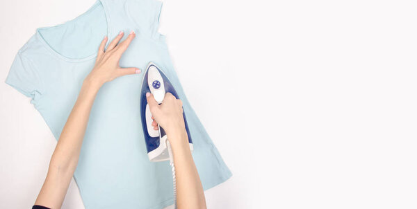 Синий утюг в руке голубая рубашка на гладильной доске, вид сверху, дом
