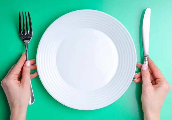 Plaat vork mes in hand op groene achtergrond — Stockfoto