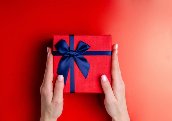 Red box gift with blue ribbon in hand on red background