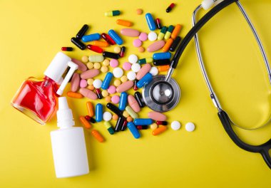 Hap kapsül termometre stetoskop burun boğaz sprey öksürük şurubu tıp sağlık üzerinde sarı arka plan üstten görünüm