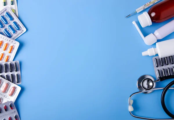 Hap kapsül termometre stetoskop burun boğaz spreyi öksürük şurubu tıp sağlık üzerinde mavi arka plan üstten görünüm — Stok fotoğraf