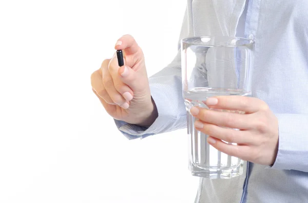 Comprimido da cápsula preta e vidro de medicina da água na mão da mulher — Fotografia de Stock