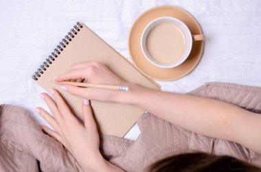 Beyaz yatak fincan kahve kadın elinde defter kalem