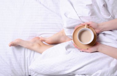 Beyaz çarşaflar yatakta kahve tutan kadın