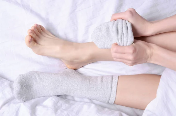 Patas femeninas en calcetines grises blancos en cama de lino blanco — Foto de Stock