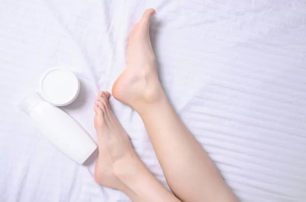 Gambe femminili piedi tallone piede bianco vaso crema nel letto bianco — Foto Stock