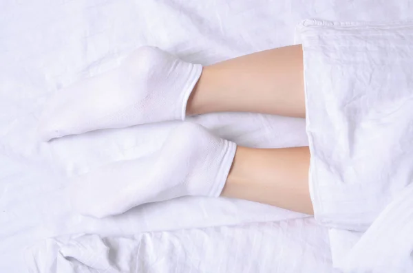 Female legs in white socks in white linens bed