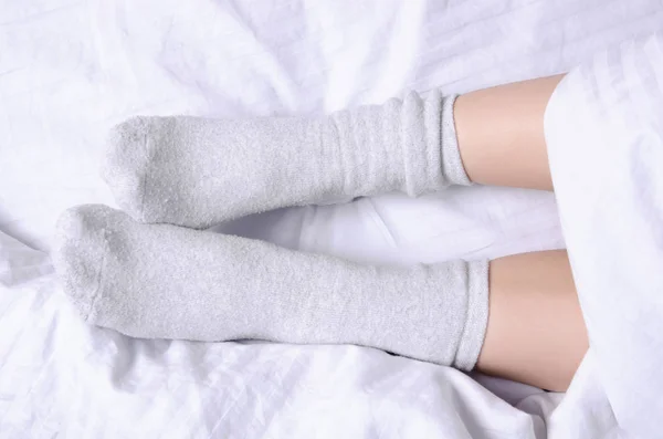 Female legs in white gray socks in white linens bed