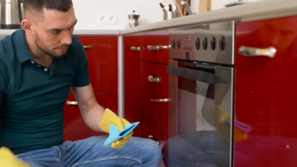 Чоловік з ганчіркою прибирає двері духовки на домашній кухні — стокове відео