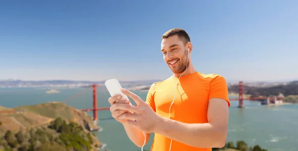 Man with smartphone and earphones over golden gate — Stock Photo, Image