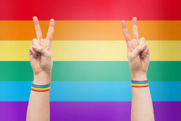 Hands with gay pride rainbow wristbands make peace — Stock Photo, Image