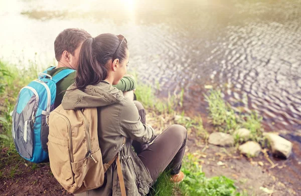 Пара з рюкзаками, що сидять на березі річки — стокове фото