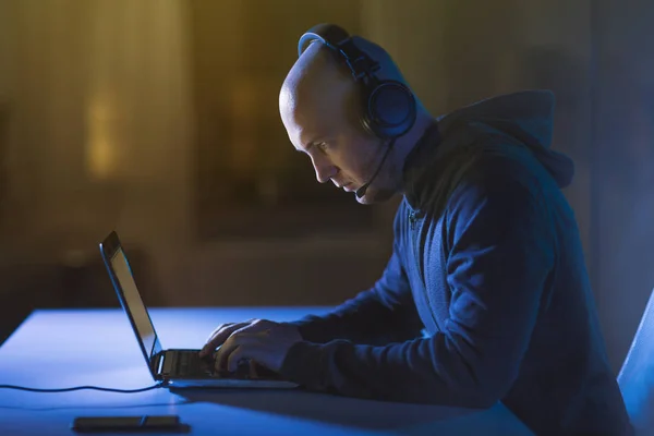 Хакер в гарнітурі, що друкує на ноутбуці в темній кімнаті — стокове фото