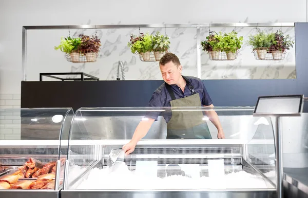 Чоловік продавець додає лід до холодильника в рибному магазині — стокове фото