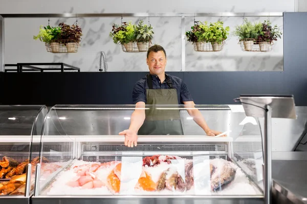 Manliga säljare visar fisk-och skaldjursrätter på fish shop kylskåp — Stockfoto