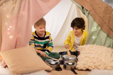 boys with pots playing music in kids tent at home clipart
