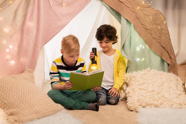 Niños felices leyendo libro en tienda de campaña de los niños en casa —  Fotos de Stock