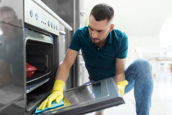 Man with rag cleaning oven door at home kitchen — Stock Photo, Image