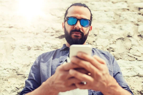 Hombre mensaje de texto en el teléfono inteligente en la pared de piedra — Foto de Stock