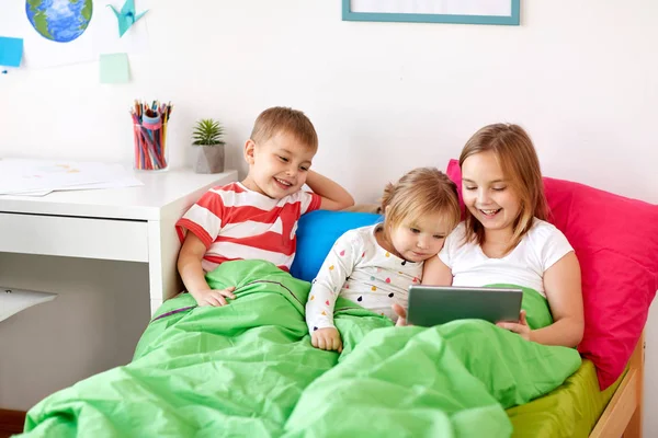 Malé děti s tablet pc v posteli doma — Stock fotografie