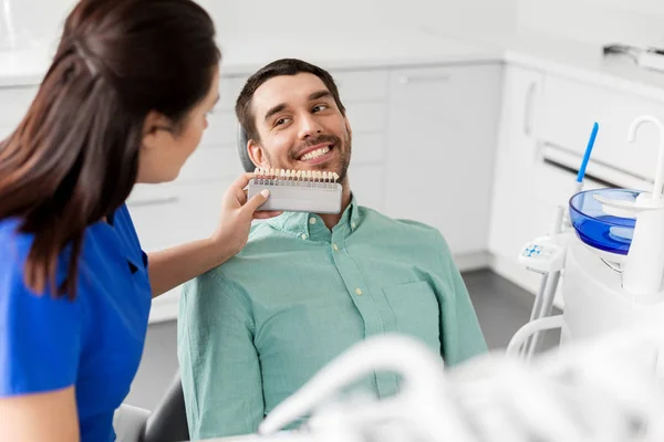 Стоматолог выбирает цвет зубов для пациента в клинике — стоковое фото