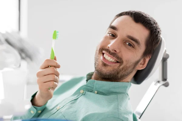Uśmiechnięty mężczyzna z szczoteczka do zębów w klinice stomatologicznej — Zdjęcie stockowe
