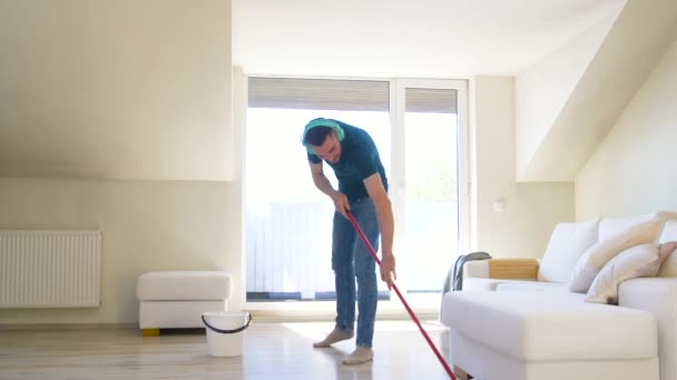 Man in hoofdtelefoons vloer schoonmaken door mop thuis — Stockvideo