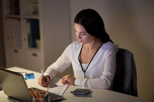 Mulher com calculadora e papéis no escritório da noite — Fotografia de Stock