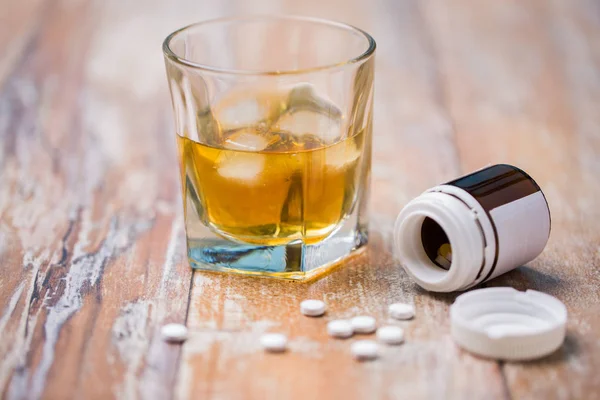 Copo de álcool e pílulas na mesa — Fotografia de Stock