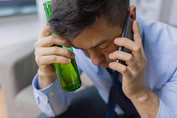 Man with bottle of alcohol calling on smartphone — Stock Photo, Image