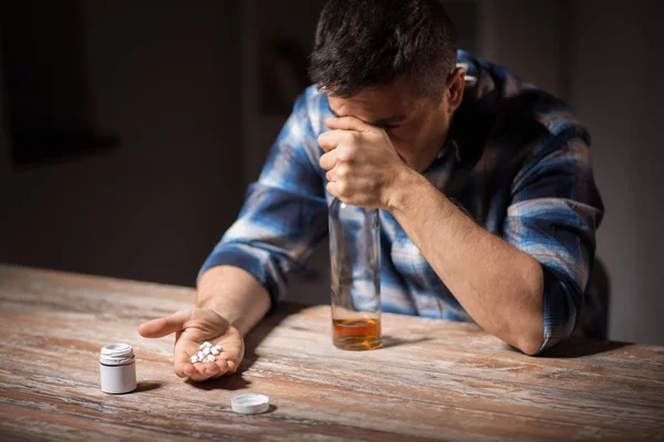 Homem bêbado infeliz com garrafa de álcool e pílulas — Fotografia de Stock