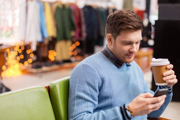 Hombre con smartphone y café en la tienda de ropa —  Fotos de Stock